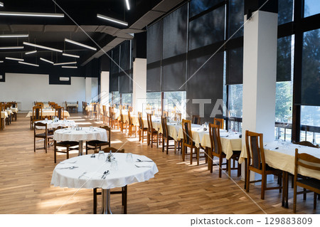 Restaurant interior with large sunlit windows and wooden chairs Restaurant interior with large sunlit windows and wooden chairs 129883809