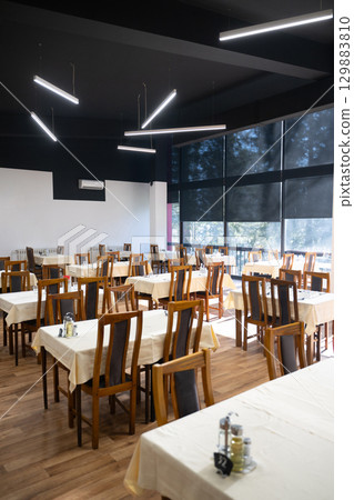 Restaurant interior with large sunlit windows and wooden chairs Restaurant interior with large sunlit windows and wooden chairs 129883810