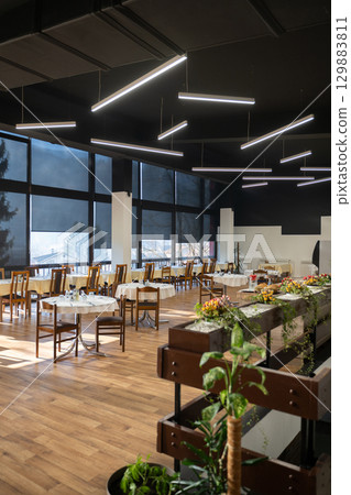 Restaurant interior with large sunlit windows and wooden chairs Restaurant interior with large sunlit windows and wooden chairs 129883811