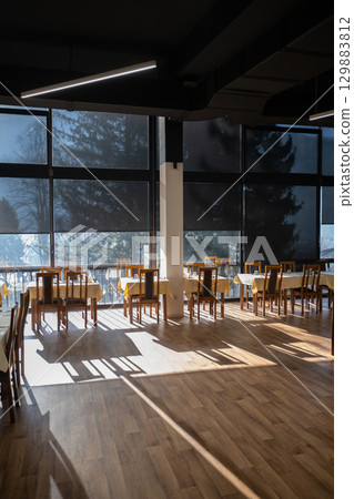 Restaurant interior with large sunlit windows and wooden chairs Restaurant interior with large sunlit windows and wooden chairs 129883812