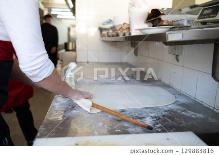 Rolling out dough on floured surface in commercial kitchen 129883816