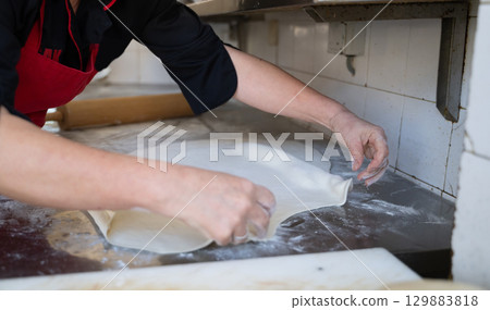 Rolling out dough on floured surface in commercial kitchen 129883818