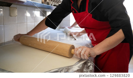 Rolling out dough on floured surface in commercial kitchen 129883820