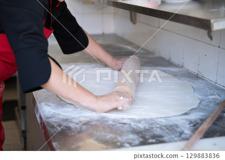 Rolling out dough on floured surface in commercial kitchen 129883836