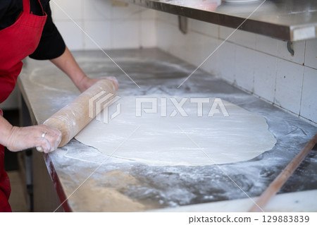Rolling out dough on floured surface in commercial kitchen 129883839