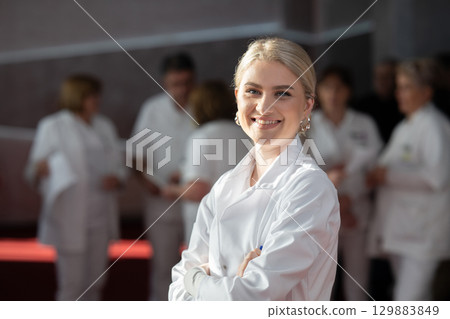 Young female doctor posing in front of medical staff Young female doctor posing in front of medical staff 129883849