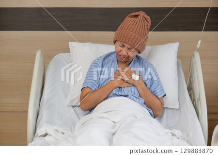 Patient in hospital bed experiencing discomfort while wearing a knitted cap in a healthcare setting 129883870