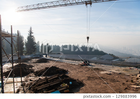 The exterior of a business building under construction is surrounded by trucks, cranes, and various construction materials, creating a bustling scene of an expansive industrial worksite in progress The exterior of a business building under construction is surrounded by trucks, cranes, and various construction materials, creating a bustling scene of an expansive industrial worksite in progress 129883996