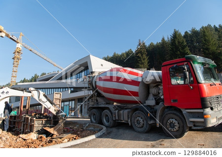 The exterior of a business building under construction is surrounded by trucks, cranes, and various construction materials, creating a bustling scene of an expansive industrial worksite in progress The exterior of a business building under construction is surrounded by trucks, cranes, and various construction materials, creating a bustling scene of an expansive industrial worksite in progress 129884016