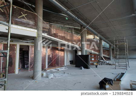 A captivating view of a modern business building under construction, showcasing its raw industrial interior with exposed steel beams and concrete walls bathed in the warm, golden hues of a sunset A captivating view of a modern business building under construction, showcasing its raw industrial interior with exposed steel beams and concrete walls bathed in the warm, golden hues of a sunset 129884028