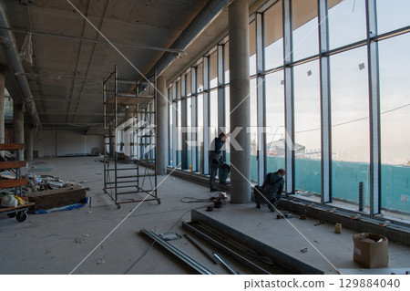 A captivating view of a modern business building under construction, showcasing its raw industrial interior with exposed steel beams and concrete walls bathed in the warm, golden hues of a sunset 129884040