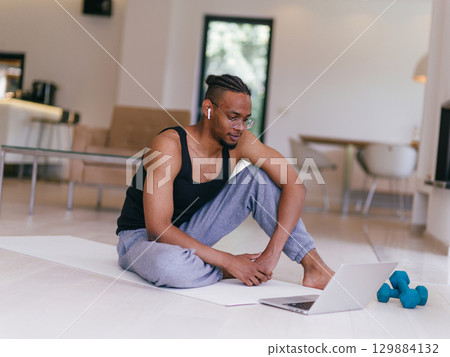 Training At Home. Sporty man doing the training while watching an online tutorial on a laptop, exercising in the living room, free space. Training At Home. Sporty man doing the training while watching an online tutorial on a laptop, exercising in the living room, free space. 129884132