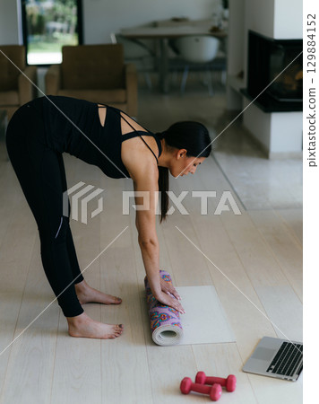 Woman in sports clothes preparing sports equipment for online training in her living room. 129884152