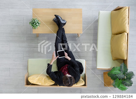 Young businessman in suit sit relax on sofa, rest his feet on the table while use tablet computer searching for interesting investment information. Top View Young businessman in suit sit relax on sofa, rest his feet on the table while use tablet computer searching for interesting investment information. Top View 129884184