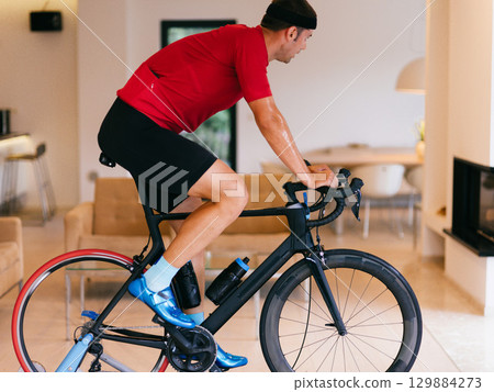Triathlete Man Cycling on Stationary Bike at Home Triathlete Man Cycling on Stationary Bike at Home 129884273