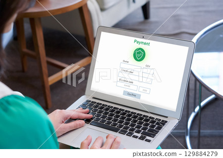 A lady is busy typing on her laptop computer which show a payment form on its screen. 129884279