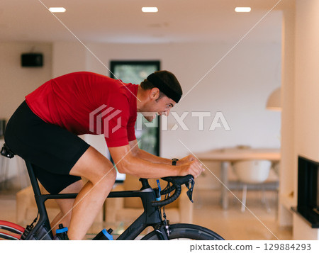 Triathlete Man Cycling on Stationary Bike at Home 129884293