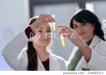 Two scientists holding test tubes with yellow liquid 129884313