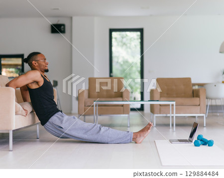 Training At Home. Sporty man doing the training while watching an online tutorial on a laptop, exercising in the living room, free space. Training At Home. Sporty man doing the training while watching an online tutorial on a laptop, exercising in the living room, free space. 129884484