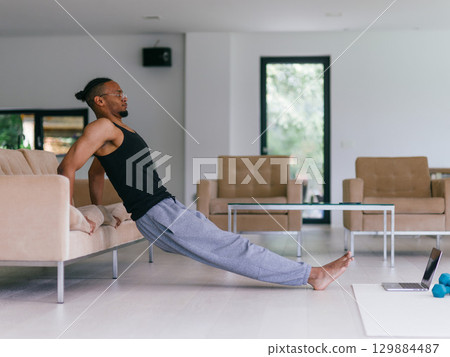 Training At Home. Sporty man doing the training while watching an online tutorial on a laptop, exercising in the living room, free space. Training At Home. Sporty man doing the training while watching an online tutorial on a laptop, exercising in the living room, free space. 129884487