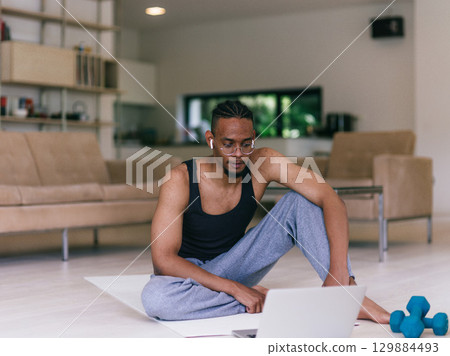 Training At Home. Sporty man doing the training while watching an online tutorial on a laptop, exercising in the living room, free space. 129884493