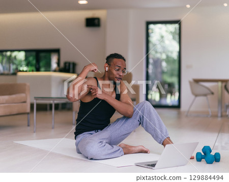 Training At Home. Sporty man doing the training while watching an online tutorial on a laptop, exercising in the living room, free space. 129884494