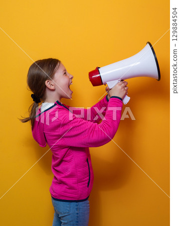 Excited girl shouting into megaphone against orange background 129884504