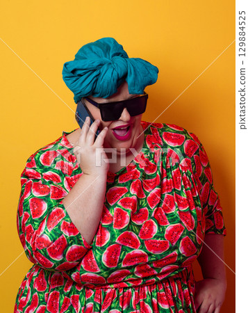 Joyful plus size woman talking on smartphone against orange background 129884525