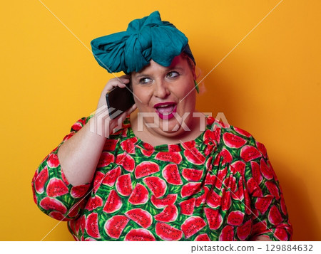 Joyful plus size woman talking on smartphone against orange background Joyful plus size woman talking on smartphone against orange background 129884632
