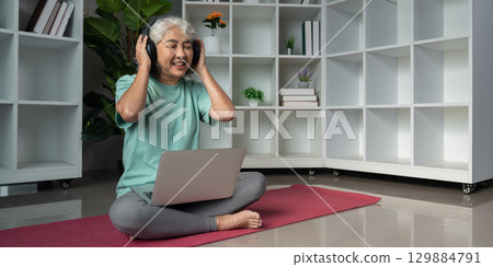 Senior Woman Enjoying Music with Headphones and Laptop in a Modern Home Setting Promoting Wellness and Relaxation 129884791