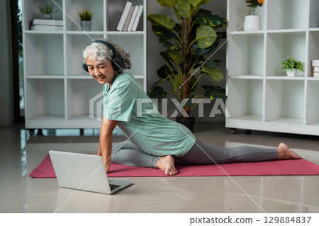 Active Senior Woman Practicing Yoga at Home for Wellness and Healthy Lifestyle with Laptop Guidance 129884837