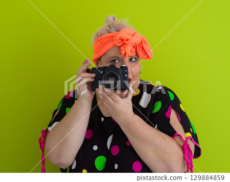 Surprised woman holding camera in front of green background 129884859