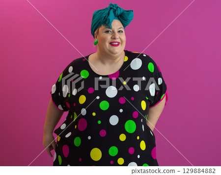 Happy plus size woman smiling in colorful outfit against pink background Happy plus size woman smiling in colorful outfit against pink background 129884882