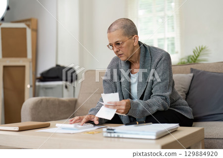 Senior Woman Planning Retirement Finances at Home with Documents and Calculator on Table Senior Woman Planning Retirement Finances at Home with Documents and Calculator on Table 129884920
