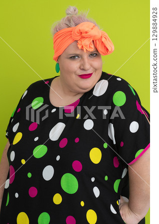 Plus size woman in vibrant polka dot outfit making a comic shrug gesture with outstretched hands and amusing expression. 129884928