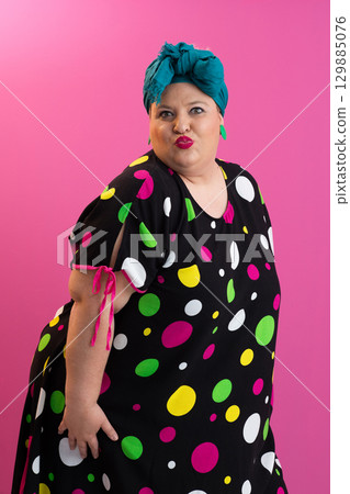 Colorful expressive big size woman posing in polka dot dress on pink background Colorful expressive big size woman posing in polka dot dress on pink background 129885076