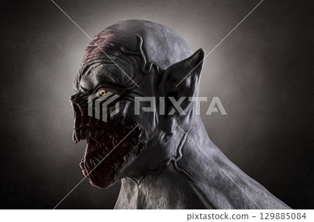 Portrait of a monster with sharp fangs over dark foggy background. Silicone mask was used in this photo. 129885084