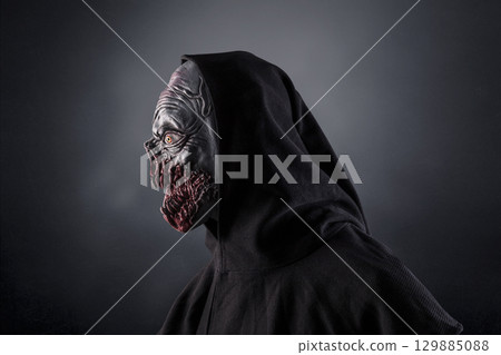 Portrait of a monster with sharp fangs with hooded cape over dark foggy background.  129885088