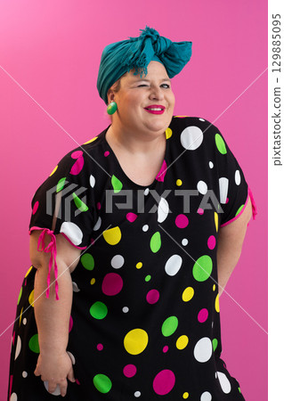 Colorful expressive big size woman posing in polka dot dress on pink background 129885095