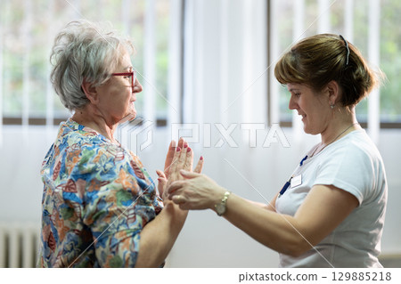Senior Physical Therapy Session.Senior woman doing physical exercises with the help of a smiling therapist. Concept of elderly rehabilitation and movement recovery. 129885218