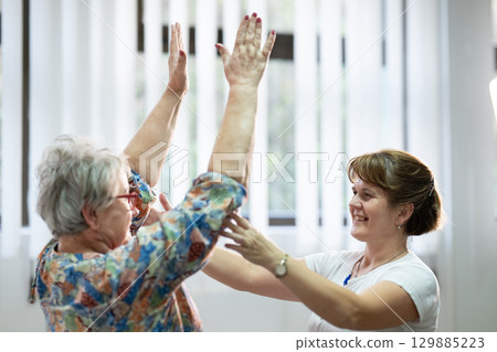Senior Physical Therapy Session.Senior woman doing physical exercises with the help of a smiling therapist. Concept of elderly rehabilitation and movement recovery. 129885223