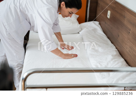 Two nurses in uniforms cleaning and organizing a hospital room by changing the bed linens and ensuring a hygienic environment for patients. Two nurses in uniforms cleaning and organizing a hospital room by changing the bed linens and ensuring a hygienic environment for patients. 129885236
