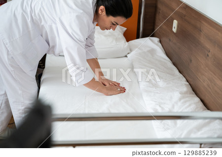 Two nurses in uniforms cleaning and organizing a hospital room by changing the bed linens and ensuring a hygienic environment for patients. Two nurses in uniforms cleaning and organizing a hospital room by changing the bed linens and ensuring a hygienic environment for patients. 129885239