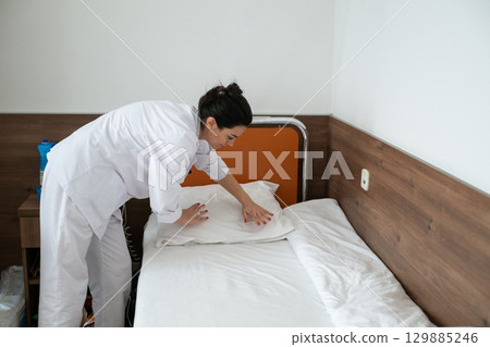 Two nurses in uniforms cleaning and organizing a hospital room by changing the bed linens and ensuring a hygienic environment for patients. Two nurses in uniforms cleaning and organizing a hospital room by changing the bed linens and ensuring a hygienic environment for patients. 129885246