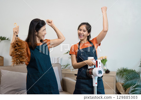 Joyful Housekeepers Engaged in Cleaning Tasks with Modern Equipment in a Cozy Home Environment 129885303