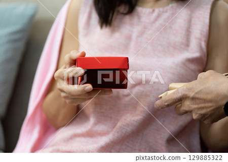 Senior Couple Celebrating Valentine's Day with Gift Exchange and Love in a Cozy Home Setting 129885322