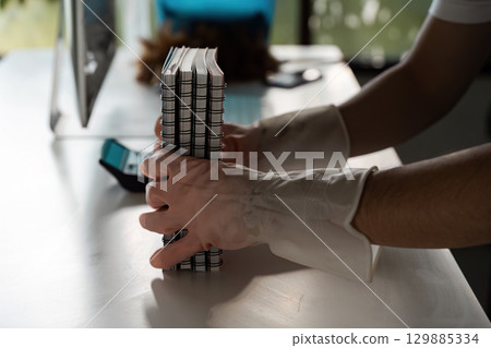 Person Wearing Gloves Organizing Notebooks on a Clean Desk in a Modern Office Environment with Natural Light 129885334