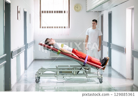 Rehabilitation with Standing Frame.Male therapist assists patient with a standing frame during a rehabilitation session in a clinical hallway. Physical recovery support concept. 129885361