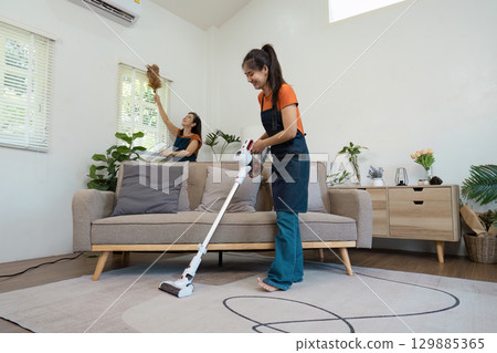 Efficient Housekeeper Vacuuming and Dusting in a Modern Living Room with Natural Light and Cozy Decor 129885365