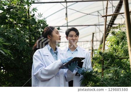 Scientists in Laboratory Coats Conducting Research in a Modern Greenhouse with Lush Green Plants and Advanced Technology 129885380